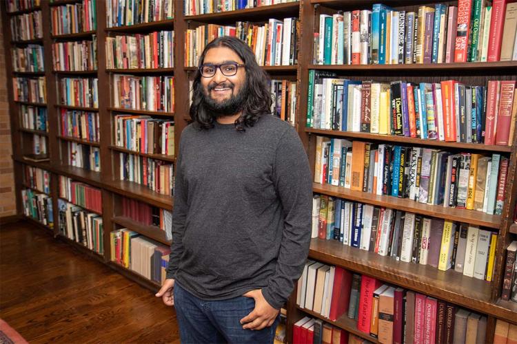 Portrait of incoming PhD student Seshu Iyengar shot in front of a row of bookshelves