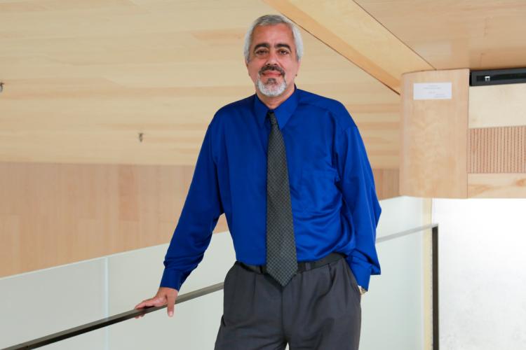 Kamran Behdinan leans on a railing, wearing a blue shirt and dark tie