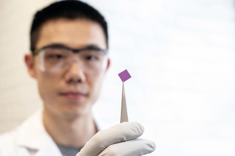 Researcher Teng Cui holds up a small pink square silicon chip that was used to stretch the graphene over