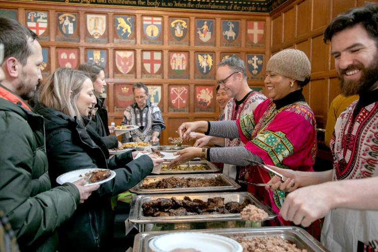 Volunteers serve lunch to eager people in line in the Great Hall at Hart House