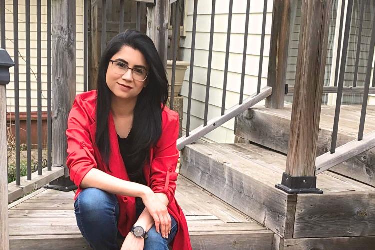 Ushma Purohit kneels on a staircase wearing a red jacket