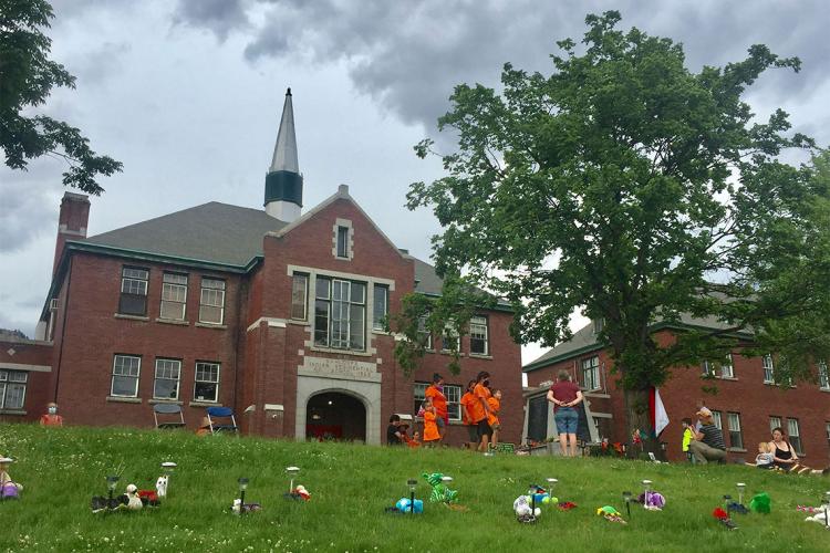 Children's shoes are placed on the ground in front of the Kamloops Residential School