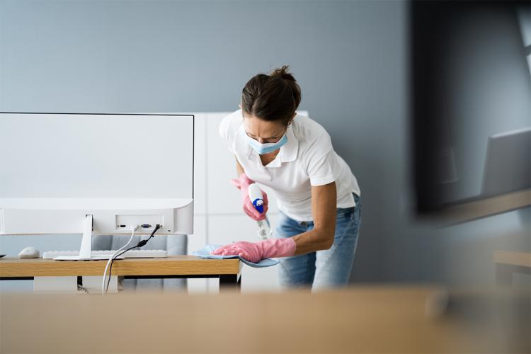 mature woman cleaning an office while wearing a surgical mask