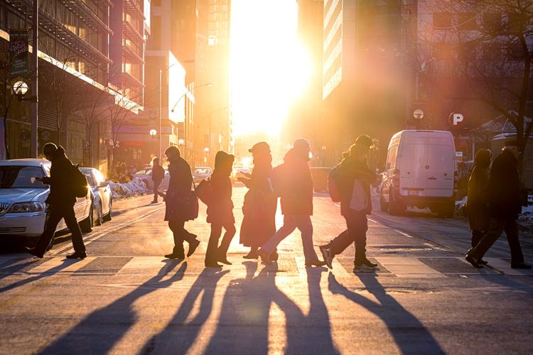 People crossing the street as the sun sets.