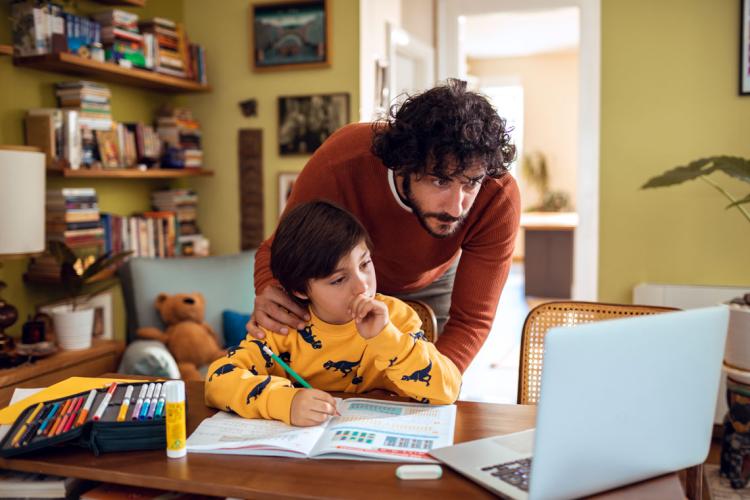 a father and son look at a laptop screen together while the son does is homework