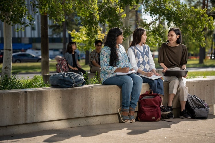 Three students sitting on a concrete bench