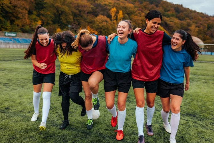 group of six young women laughing together on a sports field 