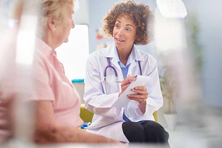 a smiling doctor writes down notes while speaking to an elderly patient