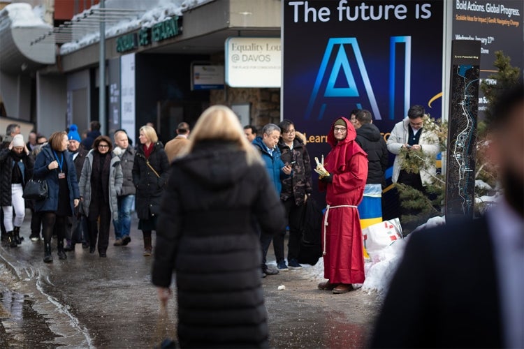 A person dressed like a monk stands in front of a sign that reads The Future is AI on a crowded street in Davos