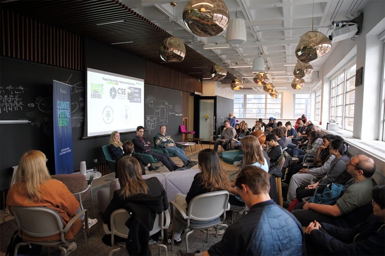 A large group of students sit in a room for the hackathon