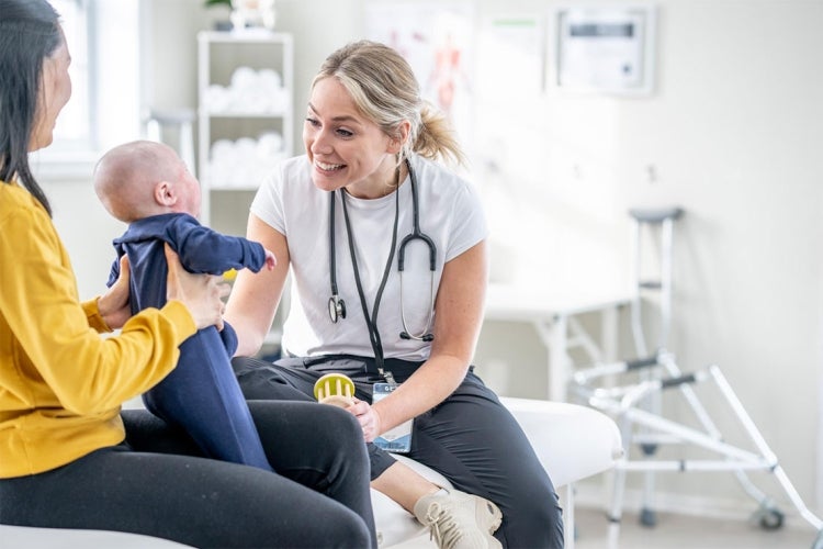 A mother holds up her infant for a nurse to examine