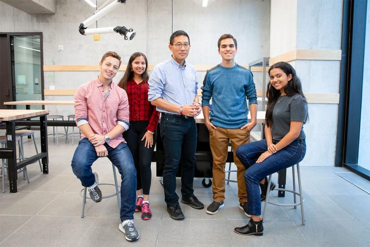 Chris Yip poses in an engineering lab with four Pearson Scholars