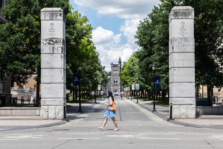 young woman walking in front of the u of t gates on college st