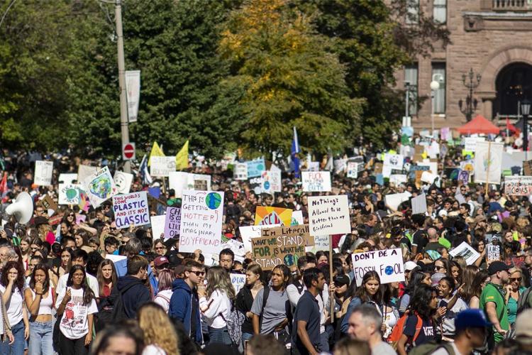 Protesters hold signs in front of Queen's Park during climate rally