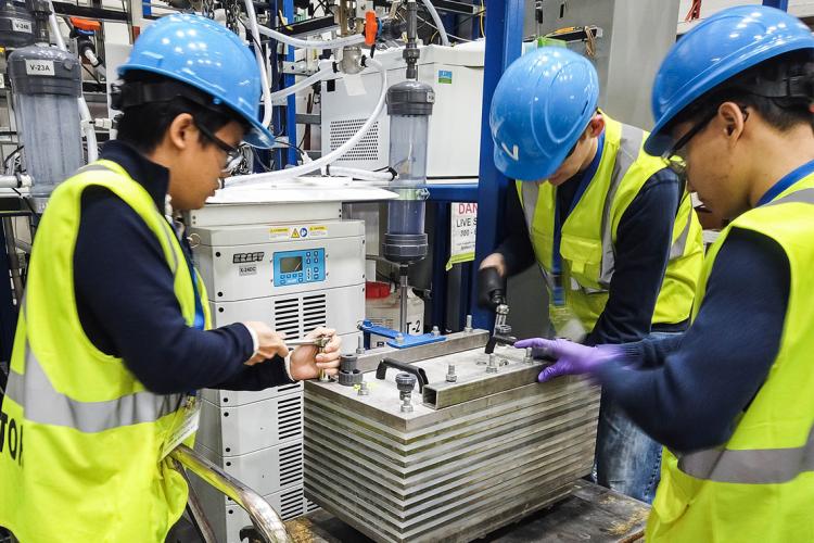 Members of the CERT team wearing blue hard hats and yellow vests work on pilot-scale electrolyzer equipment equipment 