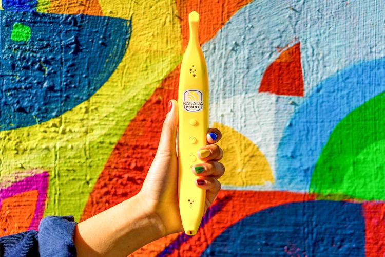 hand holding up a banana phone against a colorful outdoor wall mural