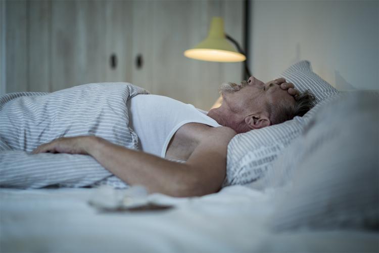 an elderly man lies in bed trying to go to sleep