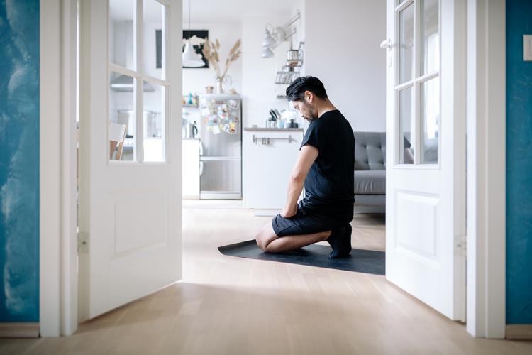 Man meditates while kneeling in his living room