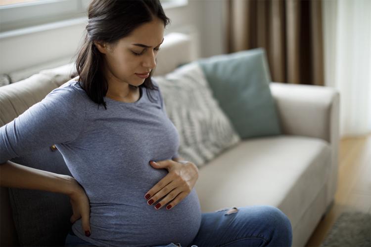pregnant woman sitting on a sofa looking in pain