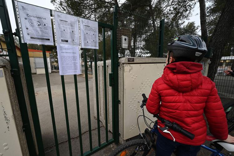 photo of a boy in a red jacket looking at a coronvirus sign hanging on a playground gate