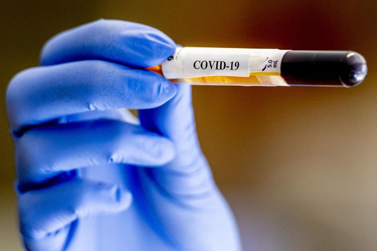 a gloved hand holds up a vial of blood that has a covid-19 label