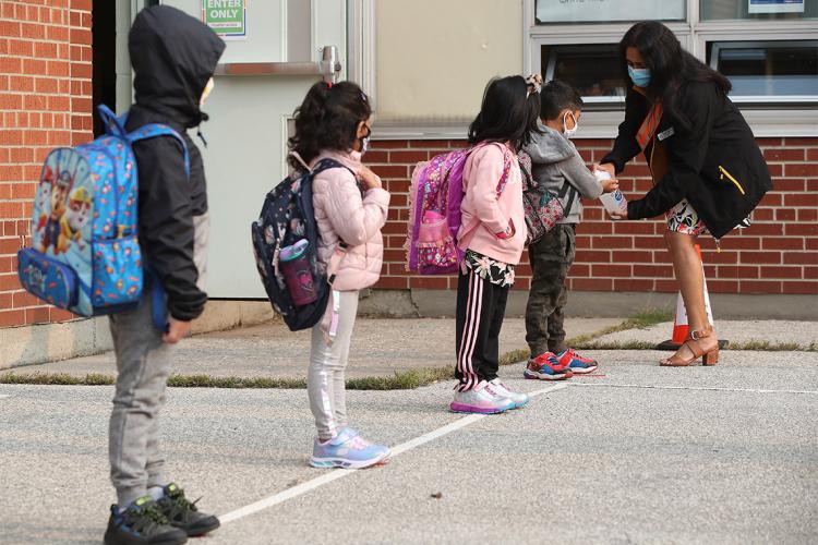 Children line up to sanitize their hands outside of an elementary school in Toronto