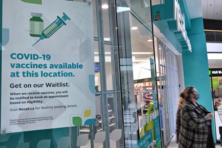 woman walks out of a Toronto pharmacy. Sign in forground reads "covid-10 vaccines available at this location"