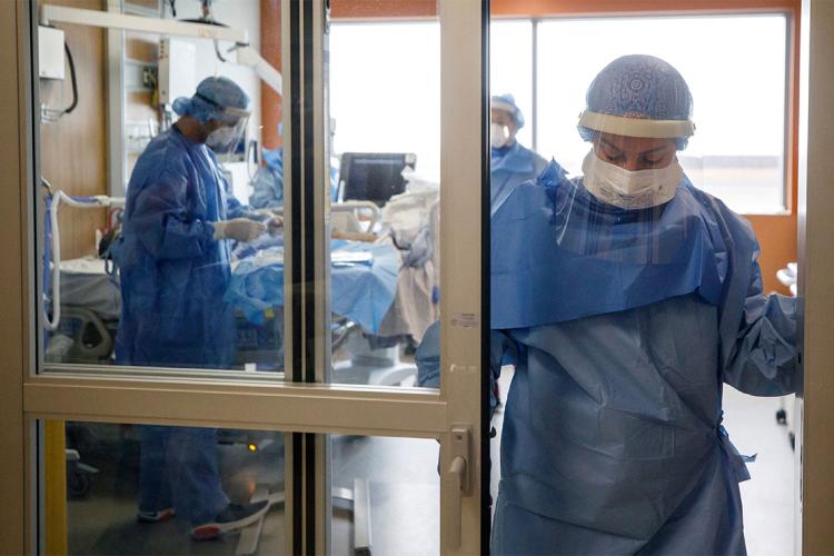 nurses attend to a covid-19 patient in a toronto hospital. one of the nurses looks tired and is leaving the room