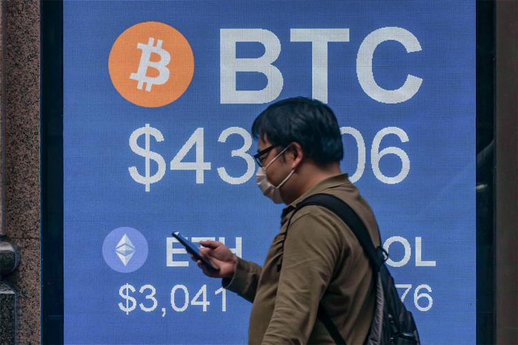 a man walks past a digital sign showing values for bitcoin and etherium cryptocurrency