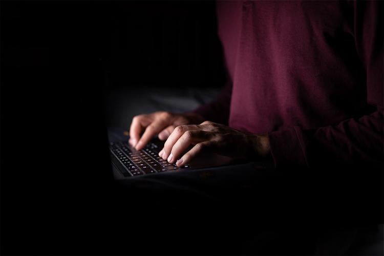 white hands typing on a laptop in a darkened room