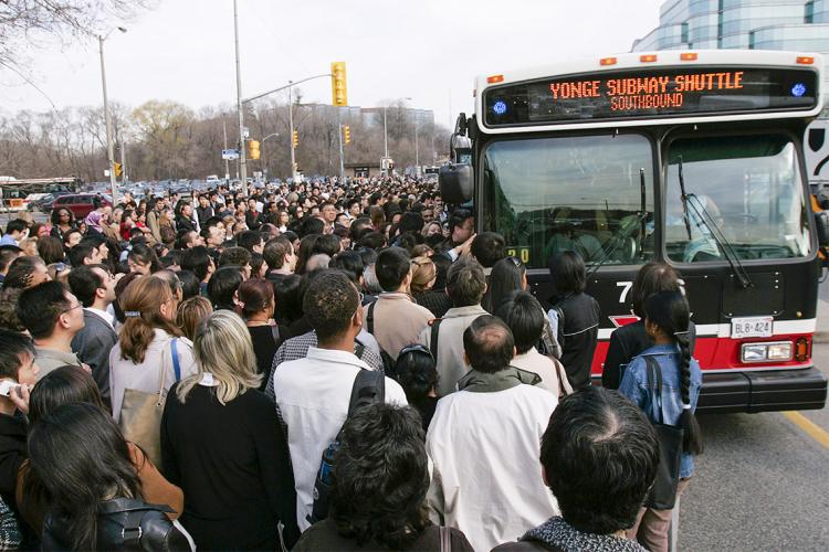 a large crowd of commuters rush a ttc shuttle bus due to a subway closure