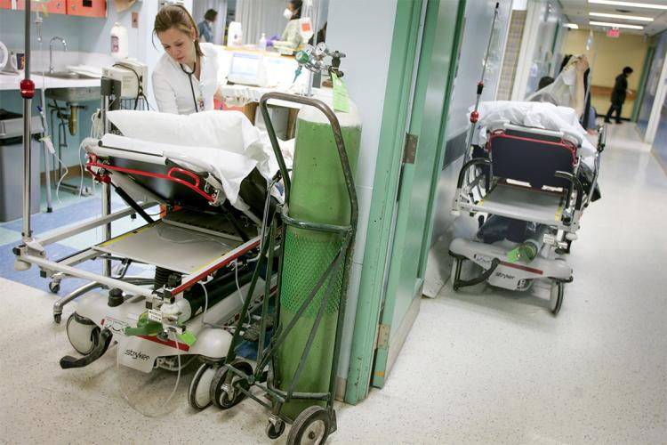 a doctor attends to an anonymous patient while another patient waits on a hospital bed in the hallway of a hospital