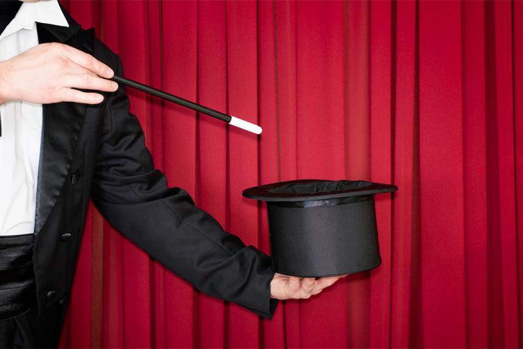 a magician points their wand at a top hat while on stage
