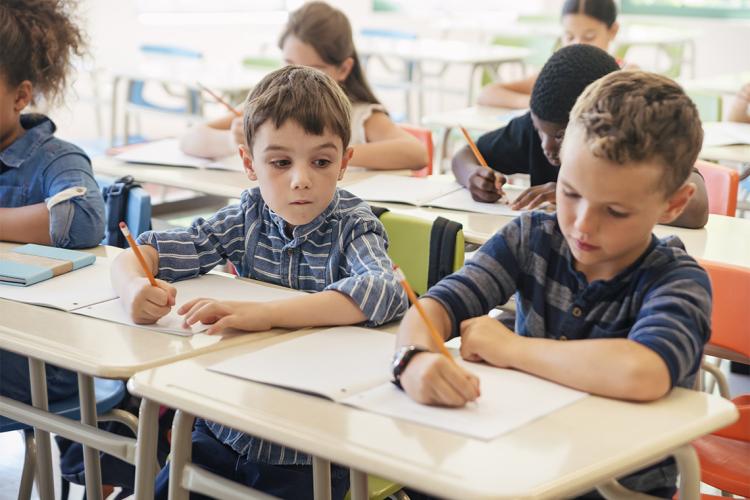 A child peers at another child's work in a classroom