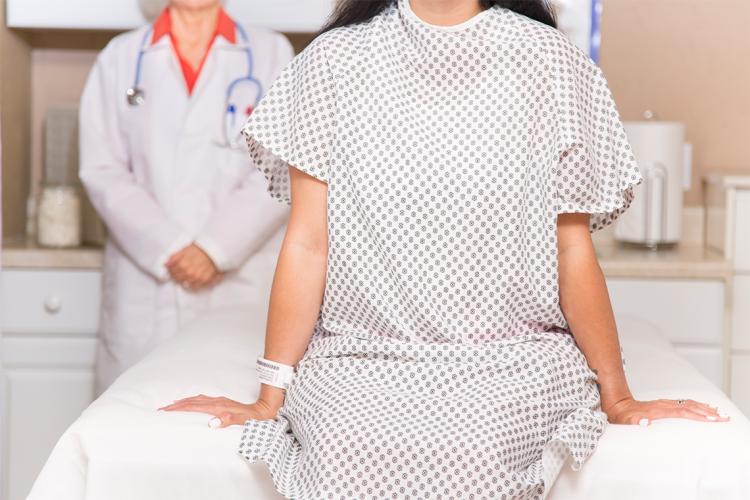 a woman in a medical gown sits on an examination table and a female doctor stands behind her