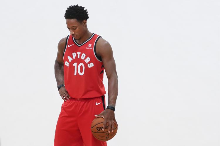 DeMar DeRozan, in a red Raptors uniform, holds a basketball at his side