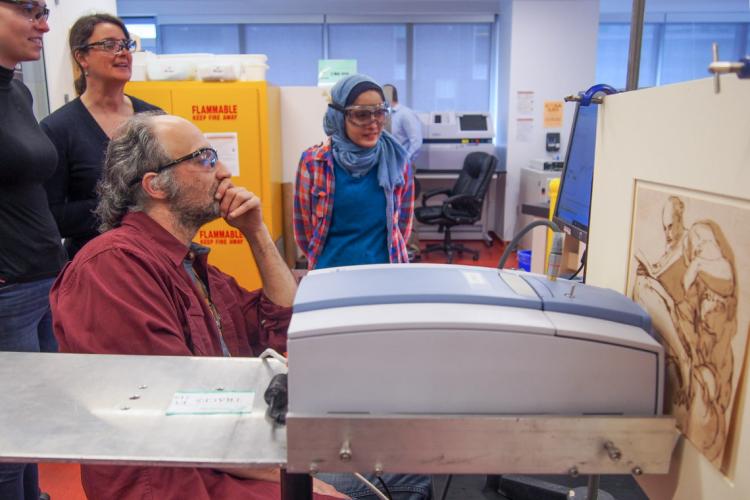 Students and researchers gather around Associate Professor Alen Hadzovic as he examines a computer screen, with a piece of artwork in the foreground