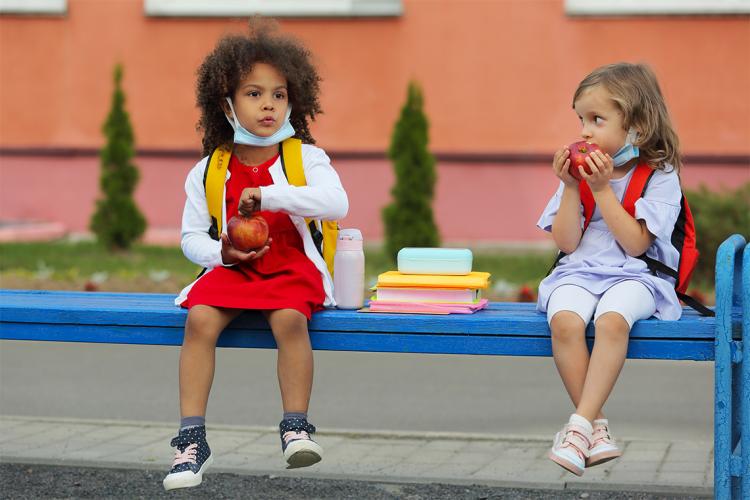 two young children sit outside to eat their lunch