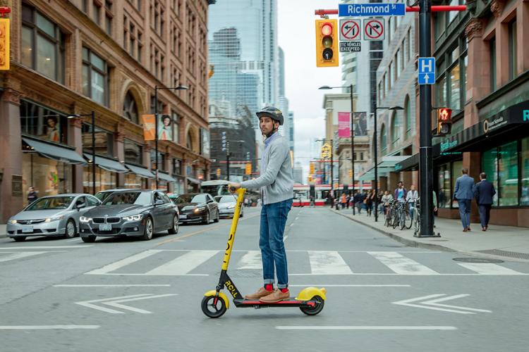 man rides a roll electric scooter in downtown toronto