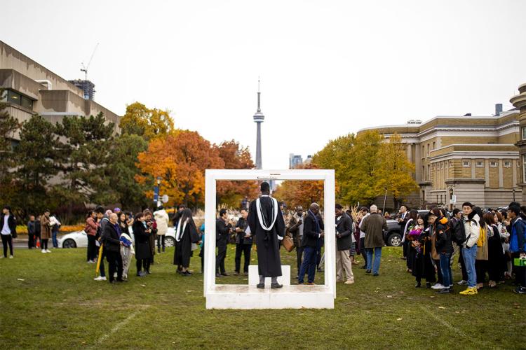 A person is posing in a large photo frame with the CN Tower is in the background