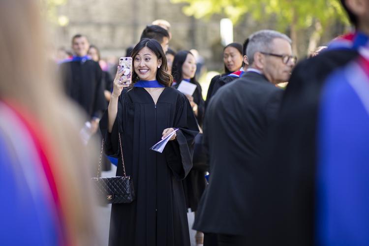 A female graduate takes a selfie outside of convocation hall