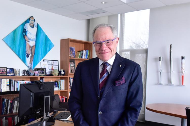 Bruce Kidd photographed in his office with his collection of olympic torches and a painting of himself