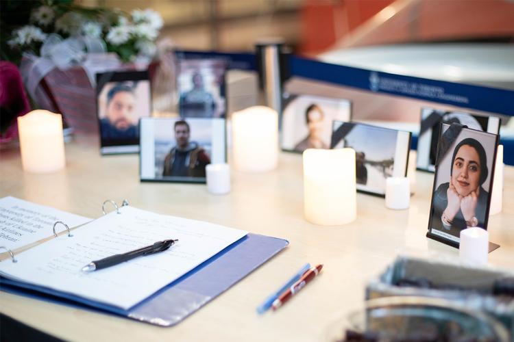 A condolence book for the victims of the PS752 plane crash is in the foreground with photos of the U of T victims in the background