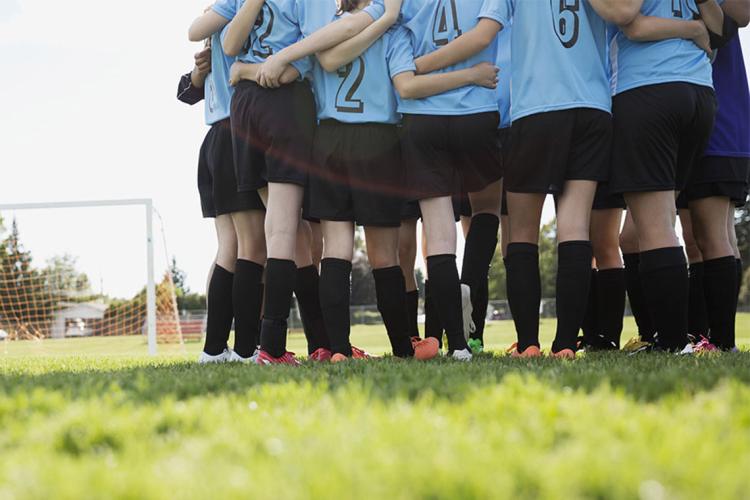 A group of young women in a huddle together on a soccer pitch
