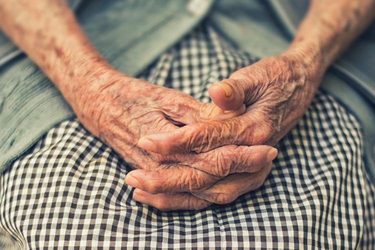 an elderly woman clasps her hands together on her lap