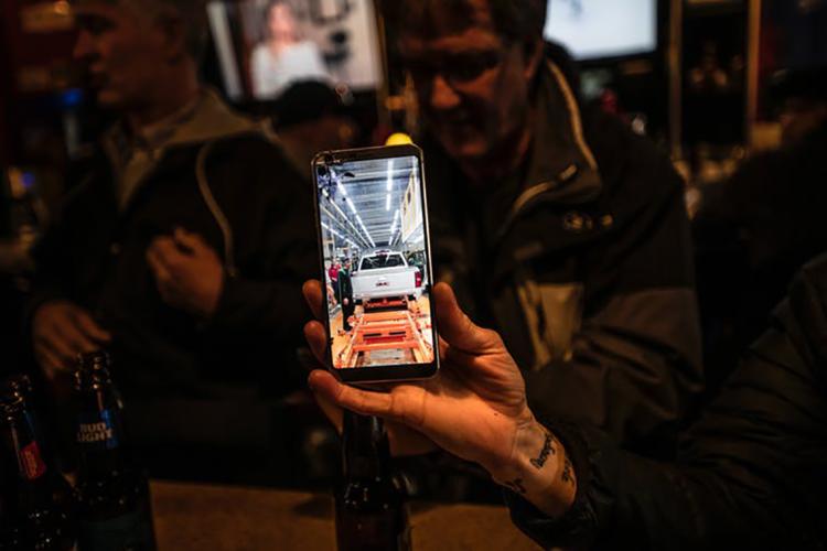 Photo of a GM worker holding an iPhone with a picture of a truck on the Oshawa plant's assembly line