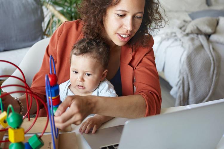 A woman plays with her child while trying to work on her laptop
