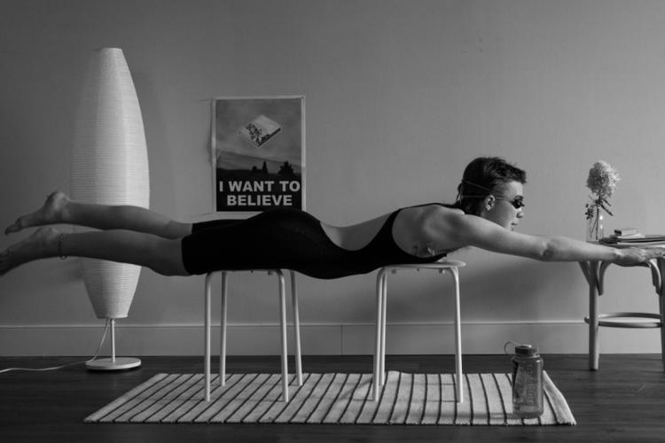 Person in a living room set on top of chairs in a horizontal position practicing swimming