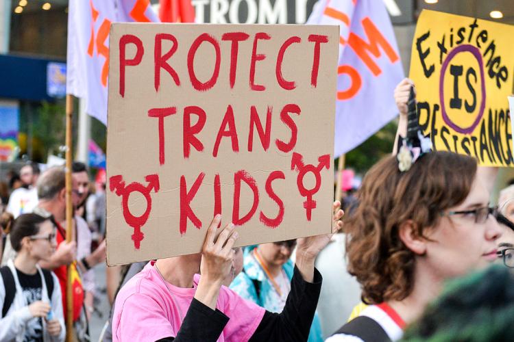 Photo of a participant in Toronto's 2019 Trans March who is holding up a sign that says "Protect Trans Kids"