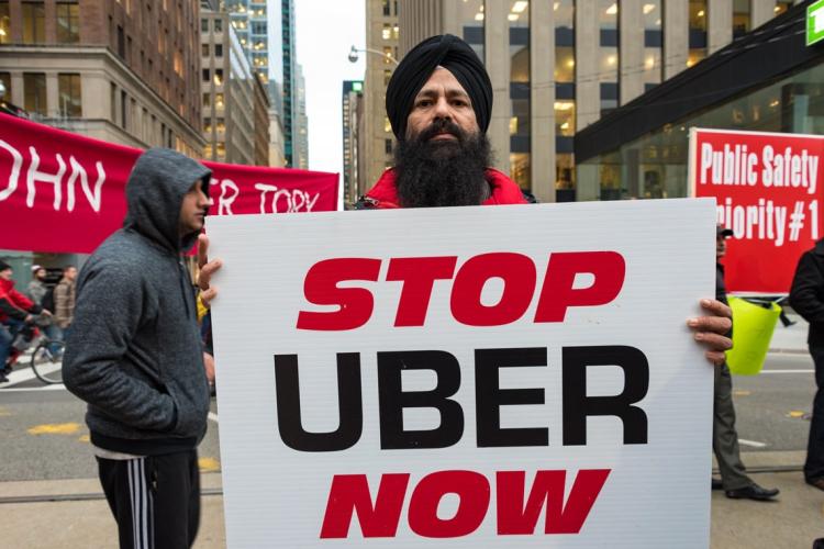 Toronto taxi driver holds a sign saying "Stop Uber Now"